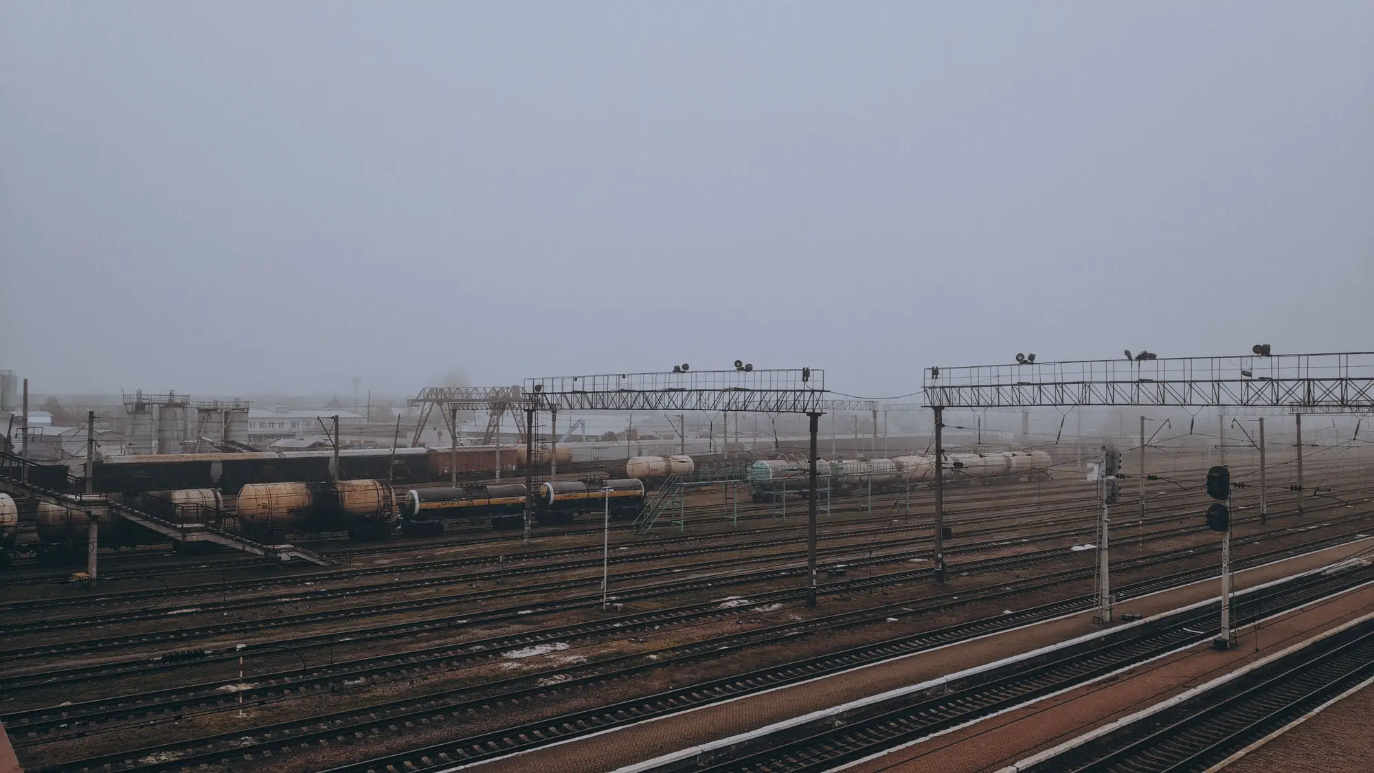 Foggy rail yard with tank wagons parked along several tracks under an overcast winter sky.